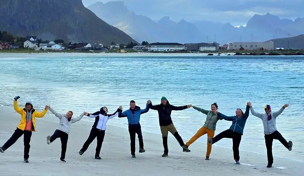 Un grup de călători Zepelin, ținându-se de mână, pe o plajă din Lofoten (Norvegia) — o vacanță reală din comunitate.